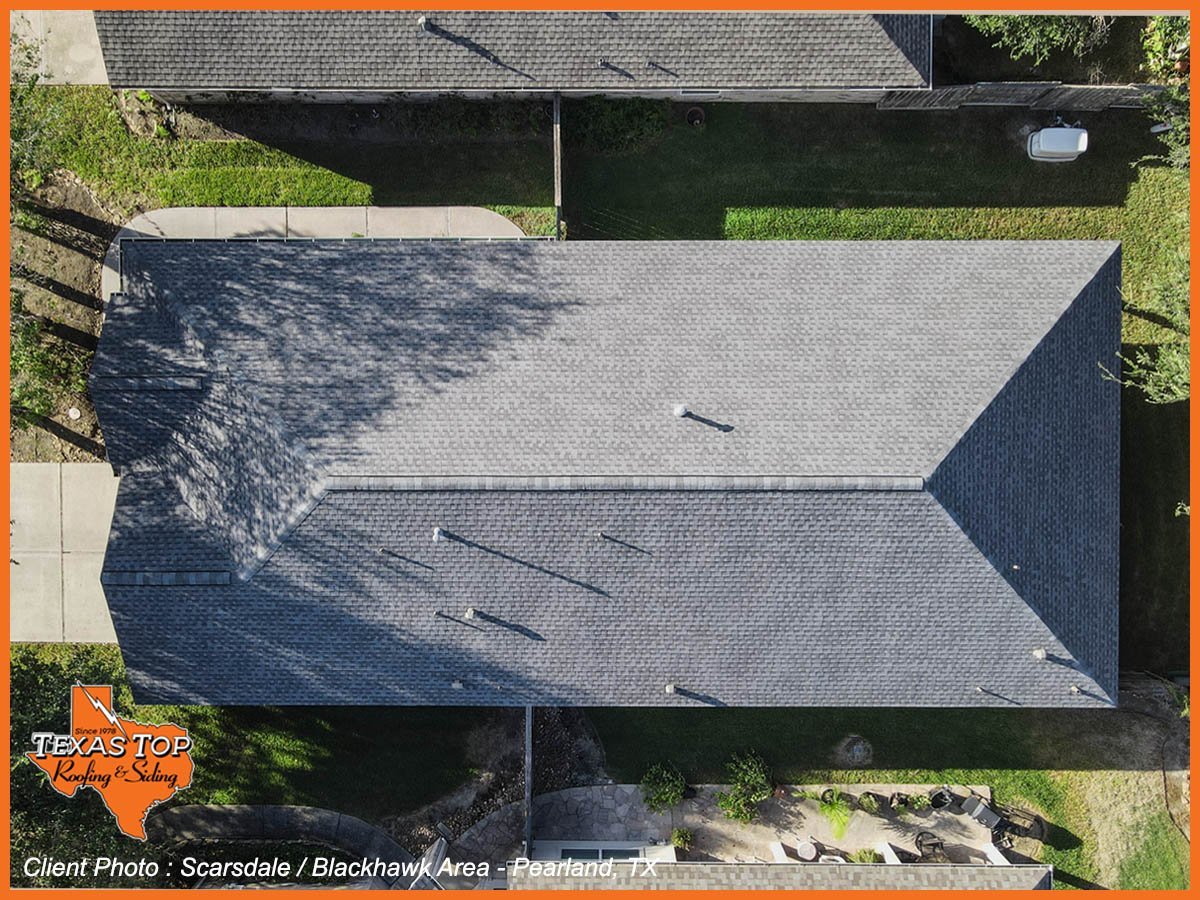Aerial view of a residential roof with asphalt shingles showing tree shadows and surrounding landscape
