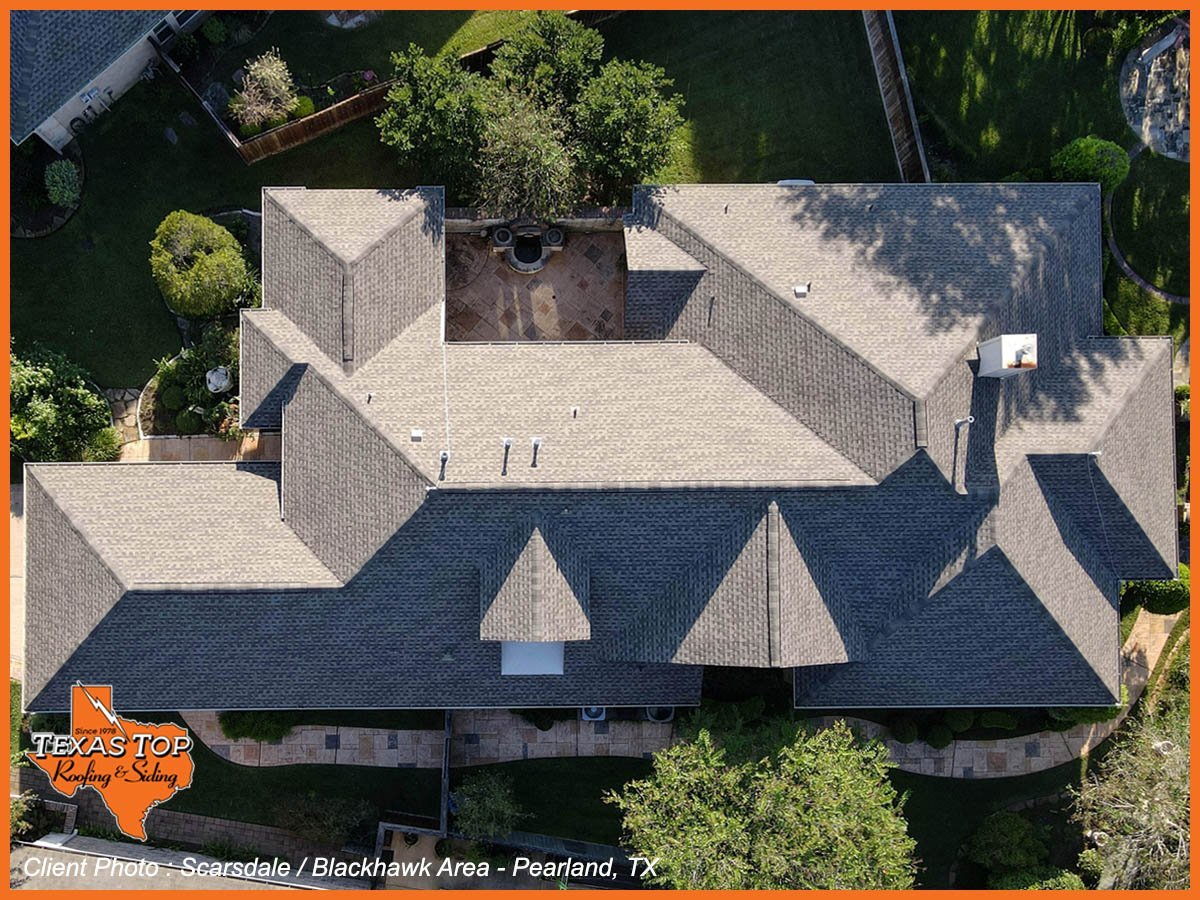Aerial view of a large brick house with dark roof and multiple chimneys surrounded by green landscaping