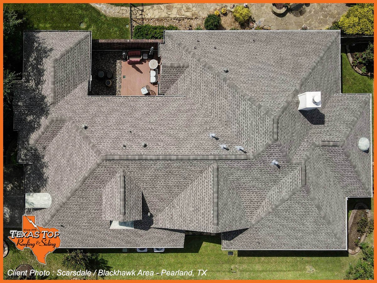 Aerial view of a residential home with dark roof and brick facade, showing driveway and surrounding landscaping in Pearland, Texas