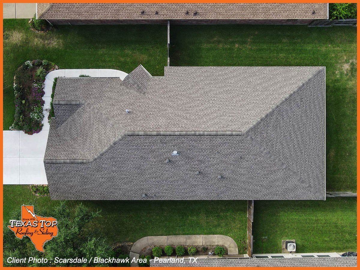Aerial view of a residential home with gray shingled roof, white trim, green lawn, and driveway in suburban Texas
